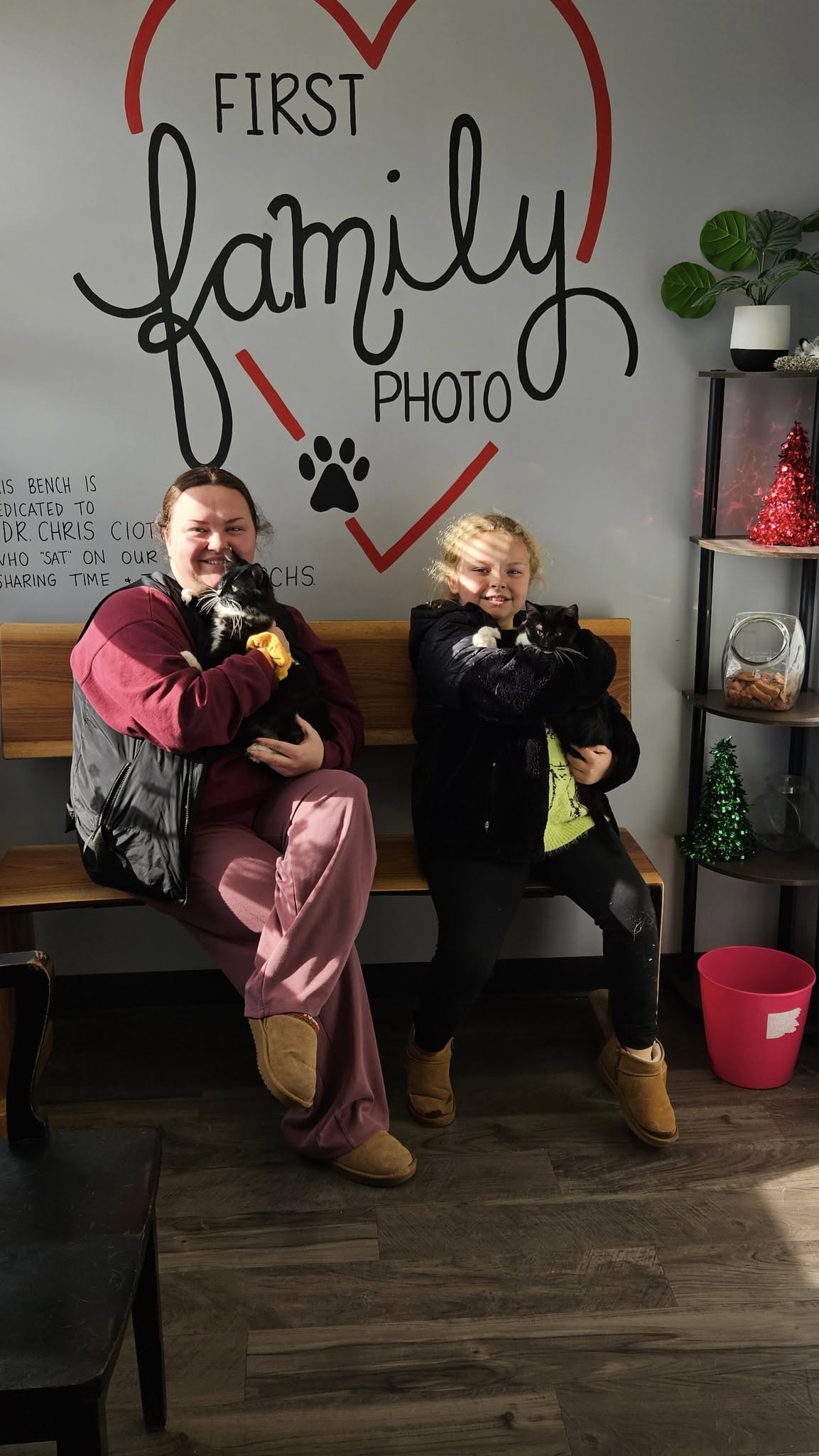 A mother and daughter taking their 'first family photo' at the shelter, each holding a newly adopted tuxedo kitten